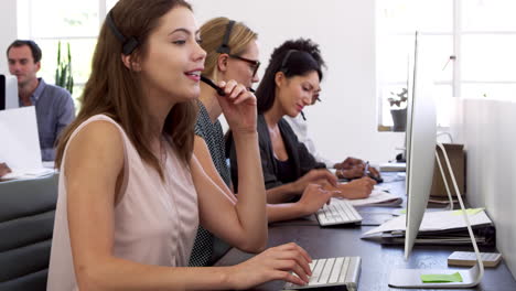 Three-women-with-headsets-on-working-at-computers-in-office