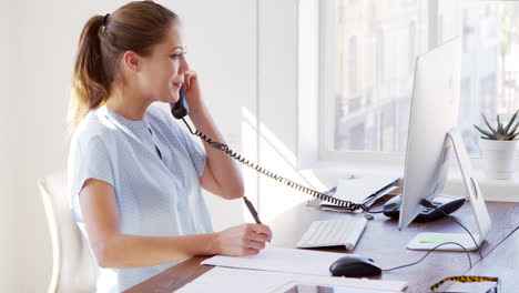 Young-white-woman-finishing-phone-call-at-her-office-desk