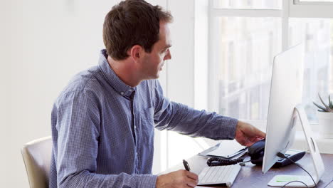 Young-white-man-using-phone-and-computer-in-an-office
