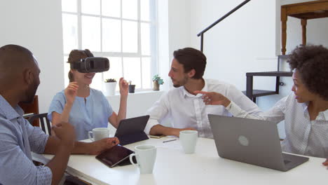 Woman-in-VR-goggles-at-a-desk-with-colleagues-in-an-office