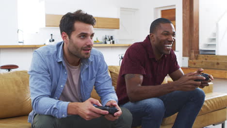 Two-Male-Friends-Sitting-On-Sofa-In-Lounge-Playing-Video-Game