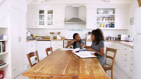Two-Sisters-Sitting-At-Table-In-Kitchen-Doing-Homework