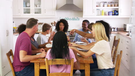 Two-Families-With-Teenage-Children-Eating-Meal-In-Kitchen