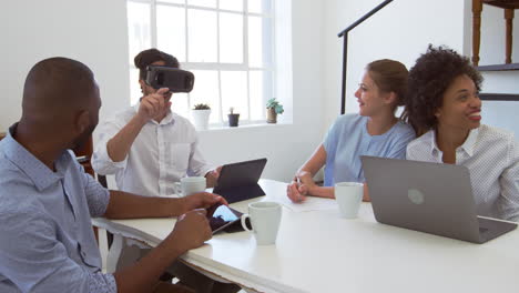 Man-in-VR-goggles-at-a-desk-with-colleagues-in-an-office