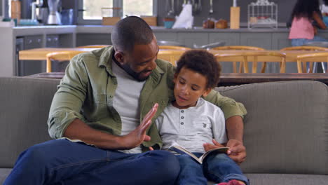 Father-And-Son-Sitting-On-Sofa-Looking-At-Counting-Book-Together