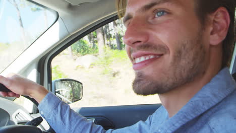 Young-smiling-man-driving-a-car-on-a-road-trip
