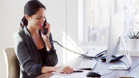 Young-Asian-woman-on-the-phone-smiling-at-her-office-desk