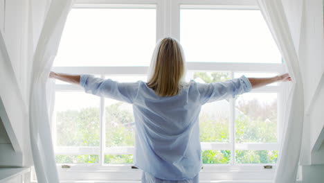 Rear-View-Of-Woman-Opening-Curtains-And-Looking-Out-Of-Window