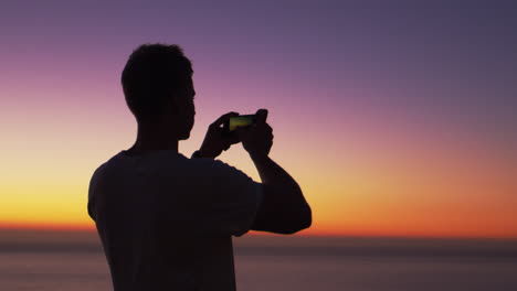 Man-taking-panorama-photo-with-phone-on-a-beach-at-sunset