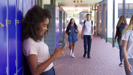 Girl-using-phone-and-boy-using-locker-in-school-corridor