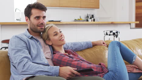 Couple-Sitting-On-Sofa-Watching-Television-Together