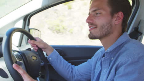 Young-smiling-man-driving-a-car-on-a-road-trip