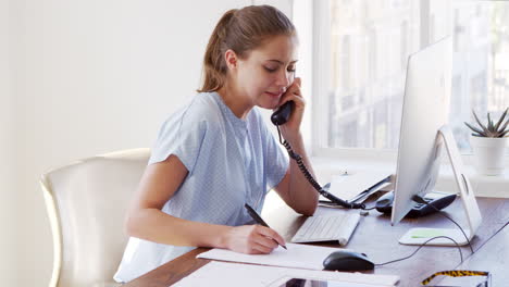Young-white-woman-on-the-phone,-smiling-at-her-office-desk