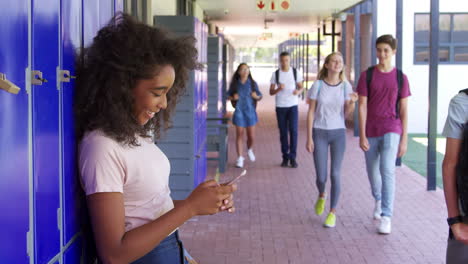 Adolescente-Negra-Usando-Un-Teléfono-Inteligente-En-El-Pasillo-De-La-Escuela