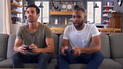 Two-Male-Friends-Sitting-On-Sofa-In-Lounge-Playing-Video-Game