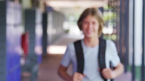 White-teenage-boy-walks-into-focus-in-high-school-corridor