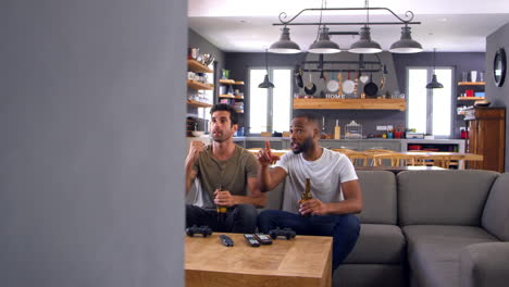 Two-Male-Friends-Sit-On-Sofa-And-Watch-Sports-On-Television