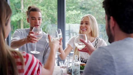 Four-young-adult-friends-celebrating-during-a-dinner-party-raise-wine-glasses-to-make-a-toast,-close-up