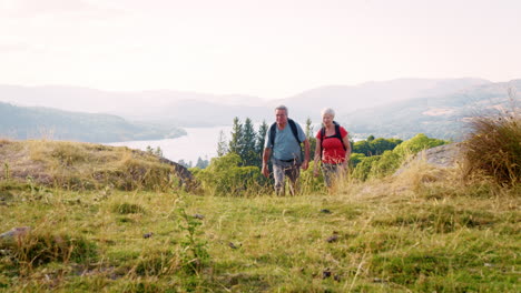 Slow-Motion-Shot-Of-Senior-Couple-Climbing-Hill-On-Hike-Through-Countryside-In-Lake-District-UK-Together