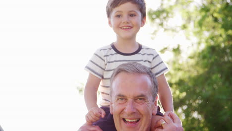 Portrait-Of-Grandfather-Giving-Grandson-Ride-On-Shoulders-In-Garden-Of-Summer-Pub