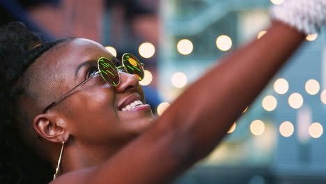 Junge-Schwarze-Frau-Mit-Runder-Sonnenbrille,-Die-Nach-Oben-Schaut,-Seitenansicht,-Kopfschuss,-Bokeh-Lichter-Im-Hintergrund