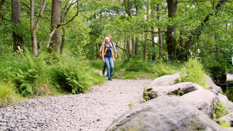 Slow-Motion-Shot-Of-Senior-Couple-Hiking-Along-Path-By-River-In-UK-Lake-District