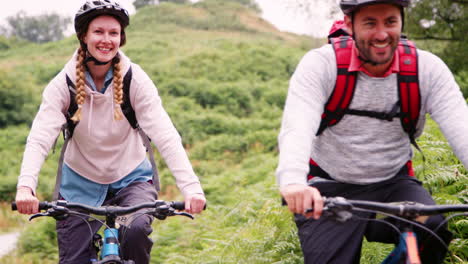 Young-adult-couple-riding-mountain-bikes-in-the-countryside-during-a-camping-holiday,-Lake-District,-UK