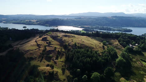 Drone-shot-of-green-hills-and-Lake-Windermere-in-sunlight,-Lake-District,-UK