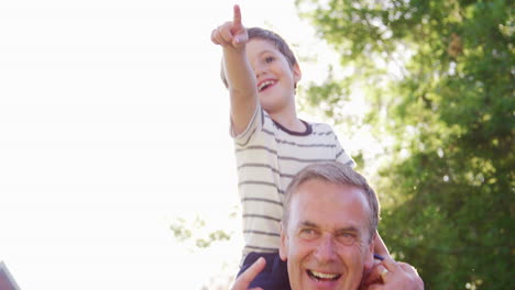 Grandfather-Giving-Grandson-Ride-On-Shoulders-In-Garden-Of-Summer-Pub