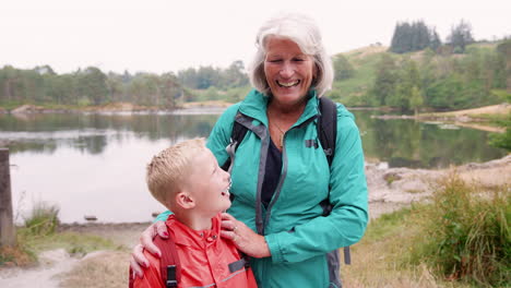 Grandmother-and-grandson-standing-together-near-a-lake-in-the-countryside-laughing,-close-up,-Lake-District,-UK