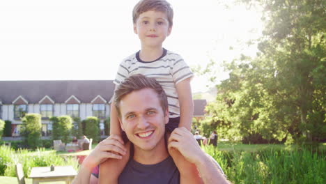 Portrait-Of-Father-Giving-Son-Ride-On-Shoulders-In-Garden-Of-Summer-Pub