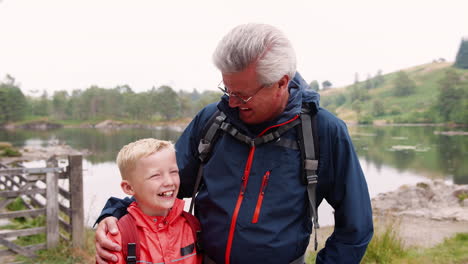 Grandfather-and-grandson-laughing,-standing-at-the-shore-of-a-lake,-close-up,-Lake-District,-UK