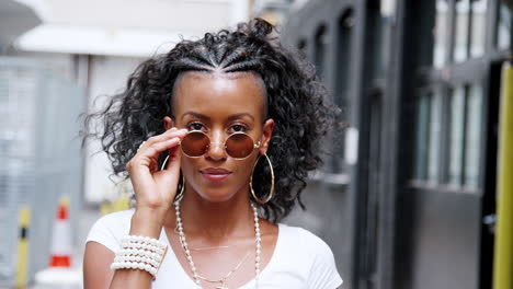 Fashionable-young-black-woman-turning-and-looking-to-camera-over-her-round--sunglasses,-close-up