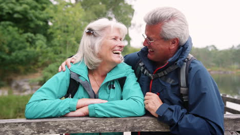 Happy-senior-couple-leaning-on-a-wooden-fence-laughing-to-camera,-close-up,-Lake-District,-UK