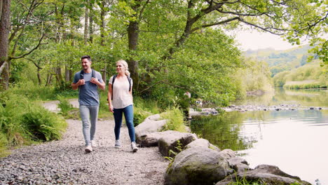 Slow-Motion-Shot-Of-Young-Couple-Hiking-Along-Path-By-River-In-UK-Lake-District