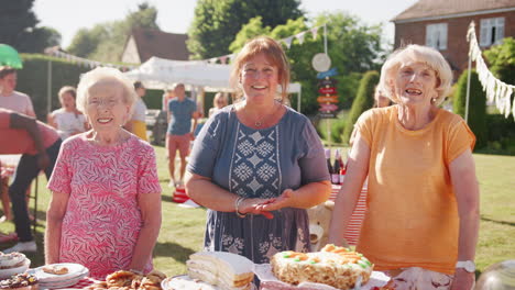 Slow-Motion-Portrait-Of-Three-Mature-Women-Serving-On-Cake-Stall-At-Busy-Summer-Garden-Fete