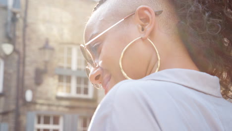 Fashionable-young-black-woman-wearing-sunglasses-talking-on-the-street,-close-up,-side-view,-lens-flare