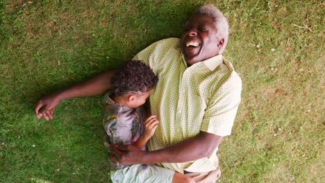 Laughing-boy-and-granddad-lying-on-grass,-overhead-close-up
