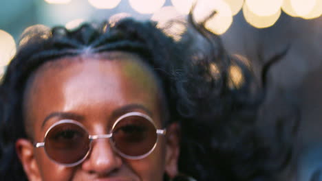 Young-black-woman-wearing-colourful-fringed-jacket-and-sunglasses-jumping-on-the-street,-close-up