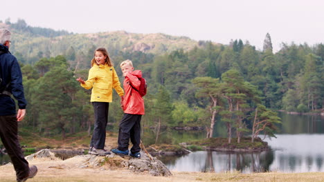Children-run-into-shot,-inviting-their-grandparents-to-admire-the-lakeside-view,-back-view,-Lake-District,-UK