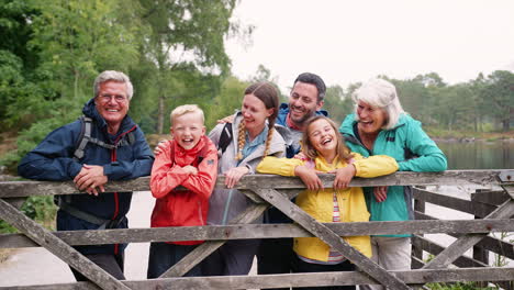 Multi-generation-family-looking-at-camera-standing-behind-wooden-fence,-Lake-District,-UK