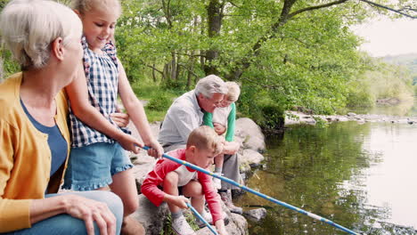 Slow-Motion-Shot-Of-Grandparents-With-Grandchildren-Sitting-On-Rocks-Fishing-With-Nets-In-River-In-UK-Lake-District