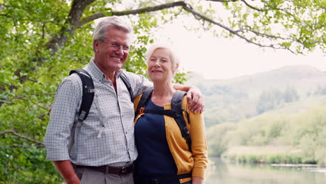Slow-Motion-Portrait-Of-Senior-Couple-Hiking-Along-Path-By-River-In-UK-Lake-District