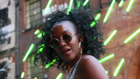 Fashionable-young-black-woman-in-urban-street-walking-to-camera-and-into-focus,-close-up,-low-angle,-blurred-neon-strip-lights-in-background