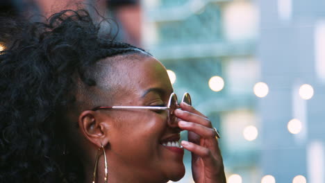 Fashionable-young-black-woman-in-sunglasses-looking-around,-head-shot,-bokeh-lights-in-background