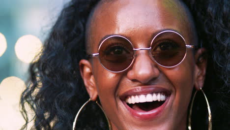 Young-black-woman-wearing-round-sunglasses-laughing,-head-shot