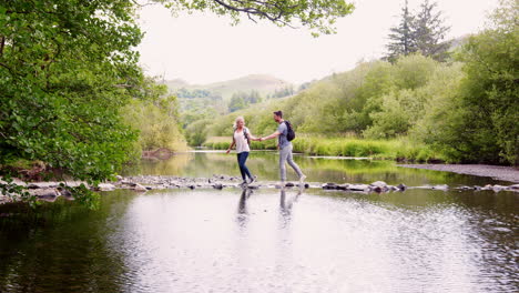 Zeitlupenaufnahme-Eines-Jungen-Paares,-Das-Beim-Wandern-Im-Britischen-Seengebiet-Trittsteine-Benutzt,-Um-Den-Fluss-Zu-überqueren