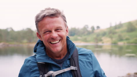 Middle-aged-man-standing-on-a-camping-holiday-standing-by-a-lake-laughing,-close-up,-Lake-District,-UK
