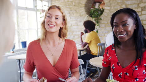 Multi-ethnic-group-of-three--female-friends-laughing-and-talking-over-brunch-in-a-busy-restaurant,-front-view,-close-up