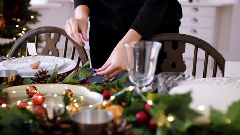 Mid-section-of-a-woman-laying-silver-cutlery-on-a-dining-table-decorated-for-Christmas-dinner,-selective-focus